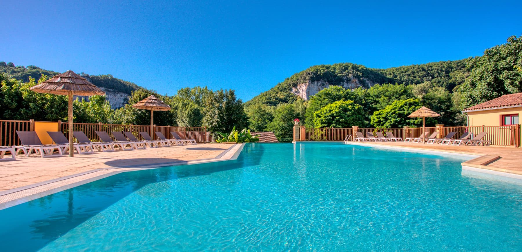 Piscine chauffée du camping La Bouysse face à la falaise, dans le Périgord Noir